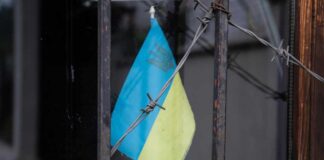 Ukrainian flag partially visible behind barbed wire in a window