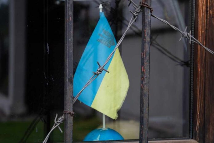 Ukrainian flag partially visible behind barbed wire in a window