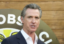 A man in a suit speaking at an outdoor event with a microphone