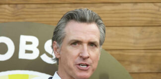 A man in a suit speaking at an outdoor event with a microphone