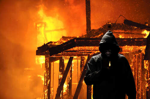 shutterstock_244348039 (1).jpg A hooded figure holding a lighter in front of a burning structure