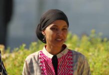 A woman in traditional attire smiling outdoors with greenery in the background