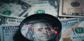 Magnifying glass over US dollar bills with stock market data displayed