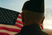 A veteran in uniform standing in front of an American flag during sunset