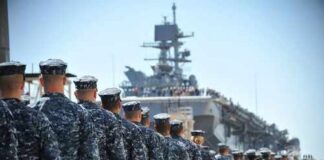 Uniformed naval personnel marching towards a ship
