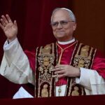 A religious leader in papal attire waving from a balcony
