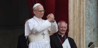 A religious leader in white robes gestures during a public address