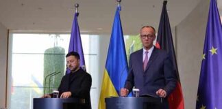 Two government officials at a press conference with flags in the background