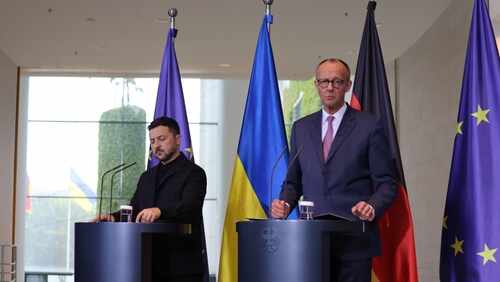 Two government officials at a press conference with flags in the background
