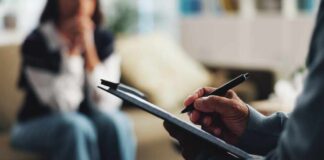 A therapist taking notes during a session with a client in the background