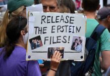 A person holding a protest sign that reads 'Release the Epstein Files' with photos attached