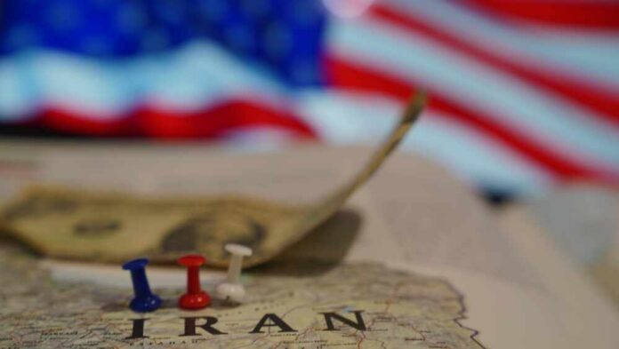 shutterstock_2725895491.jpg Map of Iran with push pins and a dollar bill in front of an American flag