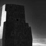 A modern architectural structure in black and white against a cloudy sky