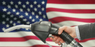 A hand holding a fuel pump in front of an American flag