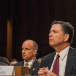 A man in a suit sitting at a table during a congressional hearing