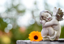 A cherub statue resting beside a bright orange flower