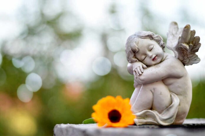 A cherub statue resting beside a bright orange flower