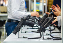 Staggering Gun Deaths Cost Each Taxpayer $1,700! Display of handguns at a firearms exhibition with attendees interacting