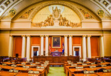 Interior view of a legislative chamber with wooden furniture and decorative ceiling