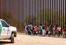 Drones of Terror: Cartels Clear Out Communities Group of families and children walking near a border wall with a customs vehicle nearby