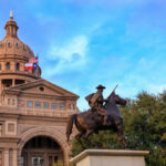 Statue of a rider in front of the Texas State Capitol building under a blue sky