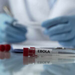 Ebola Emergency—No Vaccine, Rising Deaths! Ebola test tube on lab table with gloved researcher in background