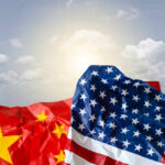 Crumpled flags of the United States and China against a cloudy sky