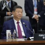 A seated leader at a conference table with a nameplate indicating the People's Republic of China