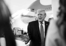 A political figure speaking outdoors in front of an airplane