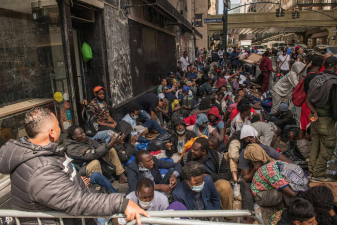 shutterstock2346880441jpg A large group of people sitting on a city street, some wearing masks, in a crowded urban setting