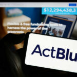 ActBlue Shielded — But What’s Hiding Underneath? A hand holding a mobile device displaying the ActBlue logo in front of a blurred screen showing fundraising information