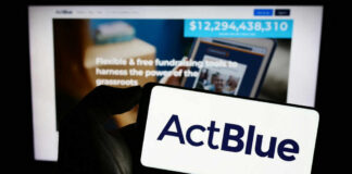 A hand holding a mobile device displaying the ActBlue logo in front of a blurred screen showing fundraising information