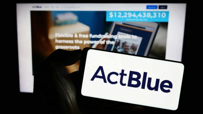 shutterstock2352242771jpg A hand holding a mobile device displaying the ActBlue logo in front of a blurred screen showing fundraising information