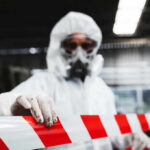 First Ebola Case Tests France’s System Worker in protective gear holding a red and white barrier tape in an industrial environment