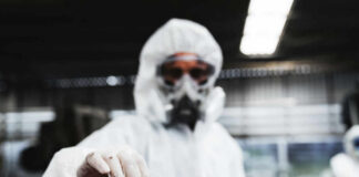 Worker in protective gear holding a red and white barrier tape in an industrial environment
