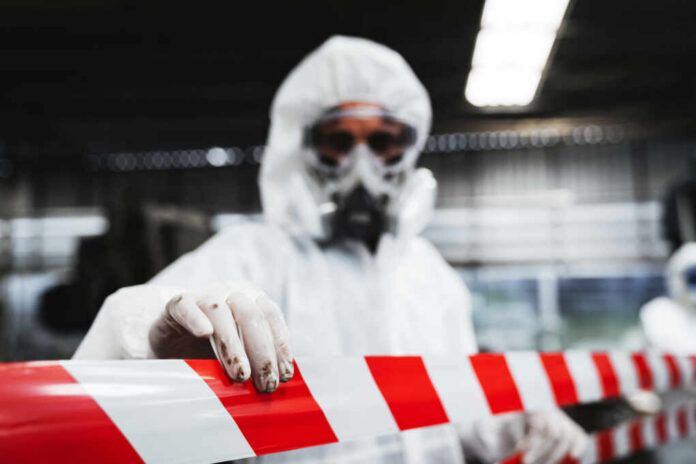 Worker in protective gear holding a red and white barrier tape in an industrial environment