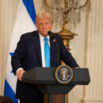 Ally Bombs Capital, Trump Erupts A political figure speaking at a podium with American and Israeli flags in the background