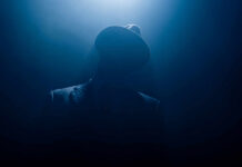Silhouetted man in fedora and suit under dramatic blue light