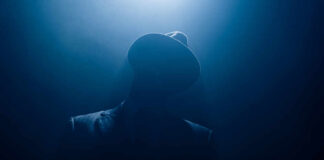 Silhouetted man in fedora and suit under dramatic blue light