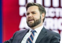 Coward Bloc Torpedoes Voter ID Push A man in a suit speaking at a conference with a colorful background