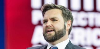 Coward Bloc Torpedoes Voter ID Push A man in a suit speaking at a conference with a colorful background