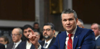 Pentagon Chief Torches Europe’s Borders A man in a blue suit speaking at a senate hearing with a panel of officials behind him