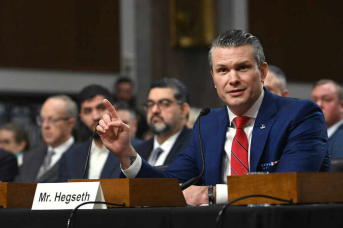 A man in a blue suit speaking at a senate hearing with a panel of officials behind him