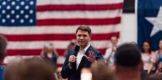 A speaker addressing an audience in front of an American flag