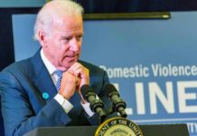 man at podium speaking with hands clasped near chin