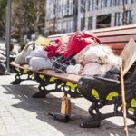 Homelessness Crackdown: Handcuffs Or Help? Person sleeping on a park bench with belongings