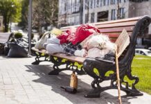 Homelessness Crackdown: Handcuffs Or Help? Person sleeping on a park bench with belongings