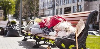 Person sleeping on a park bench with belongings