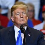 Biden Heir Targets Trump Dynasty man in suit speaking at a rally podium