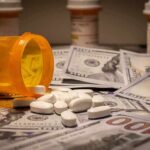 Budget Squeeze Coming For Medicare Drug Plans Prescription pill bottle and white tablets on scattered US dollar bills